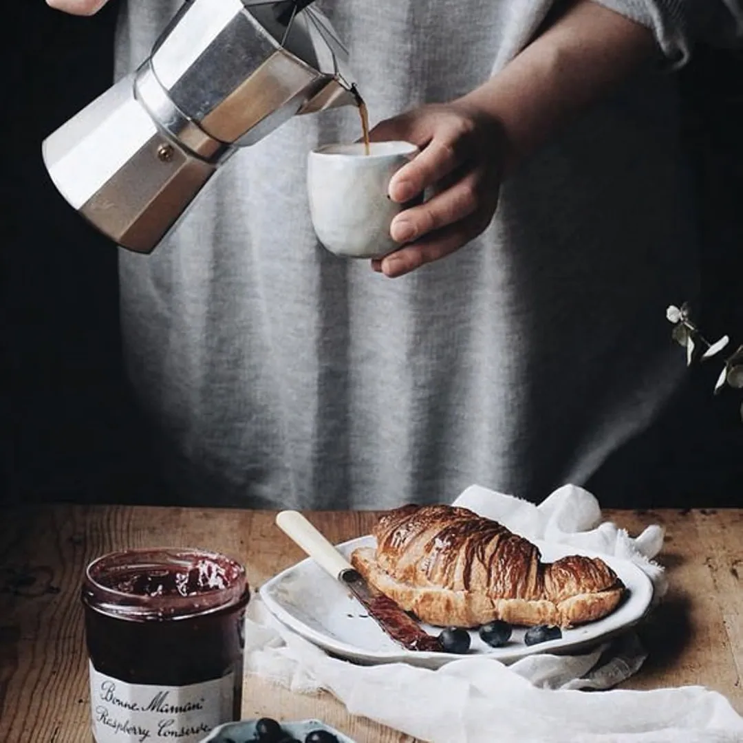 Coffee being poured beside a croissant